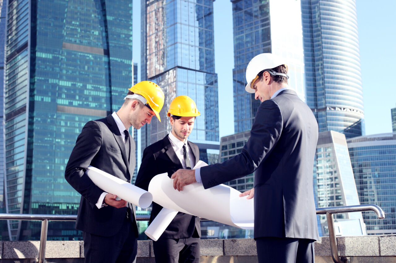 Trois ingénieurs en casques examinant des plans sur un chantier urbain.