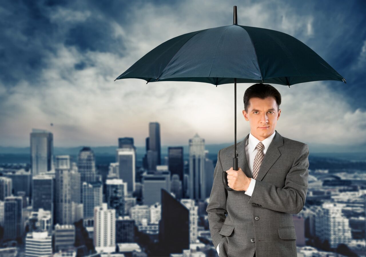Homme en costume tenant un parapluie, avec une ville en arrière-plan.