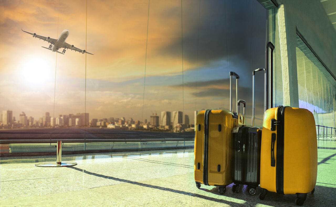 Valises jaunes prêtes à l'embarquement avec avion en vol en arrière-plan et vue sur la skyline d'une ville au coucher du soleil.
